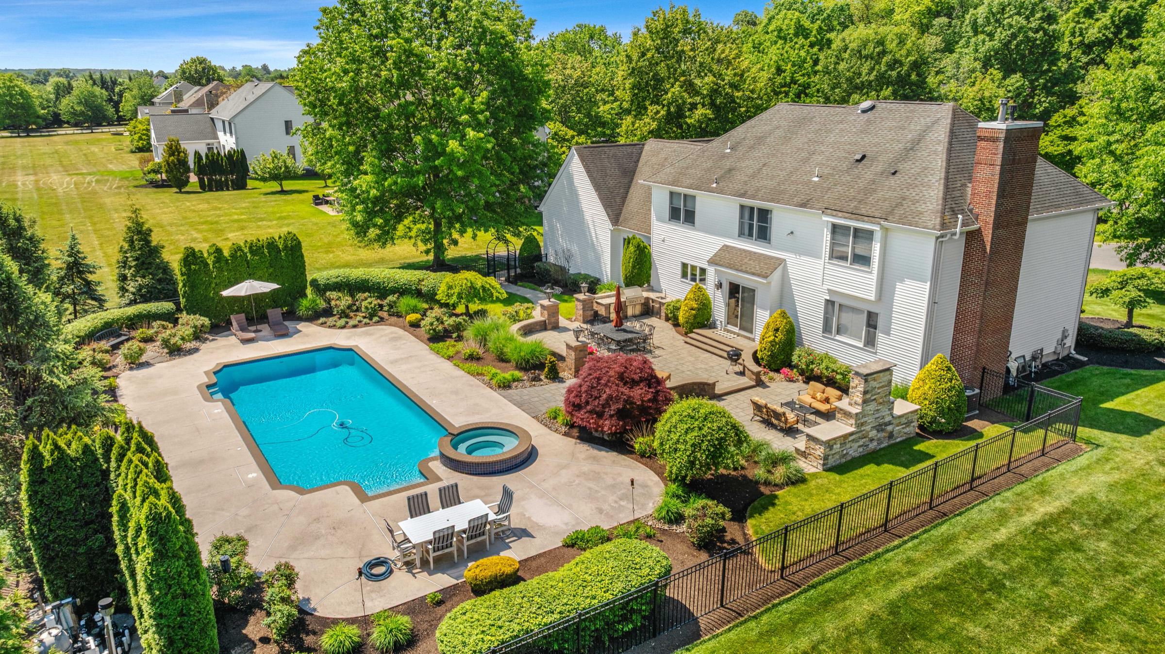 Aerial drone view of a backyard pool, patio, and landscaped grounds